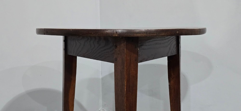 A dark brown Georgian oak cricket table featuring a circular planked top supported by three splayed tapered legs. View V