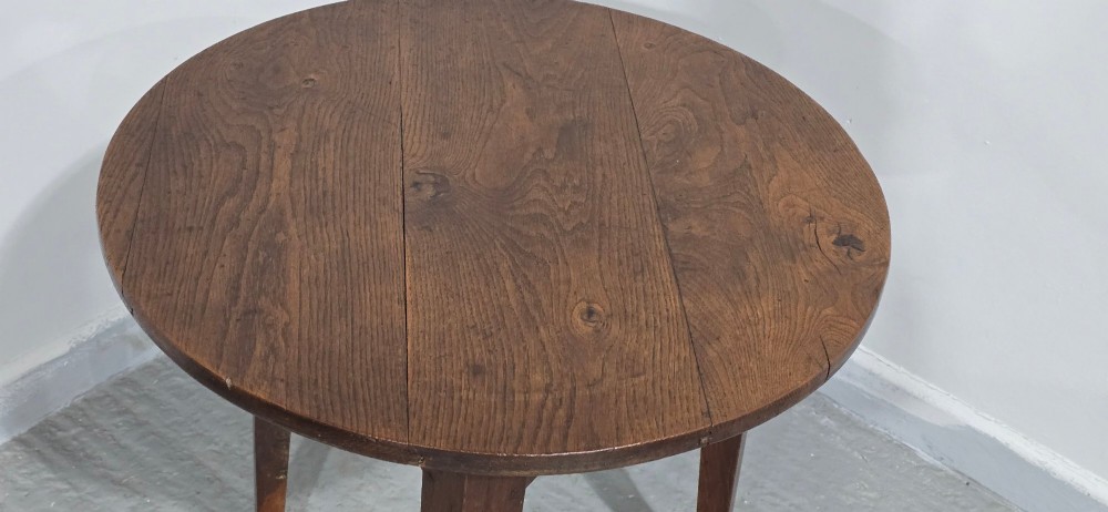 A dark brown Georgian oak cricket table featuring a circular planked top supported by three splayed tapered legs. View IX