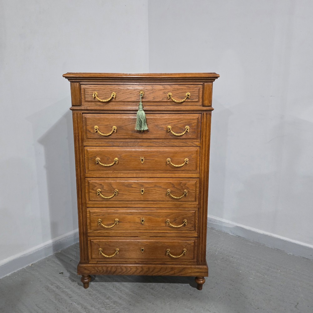 A tall French oak chest of drawers featuring six stacked drawers, brass swing handles, fluted side pilasters, and turned wooden feet. View V