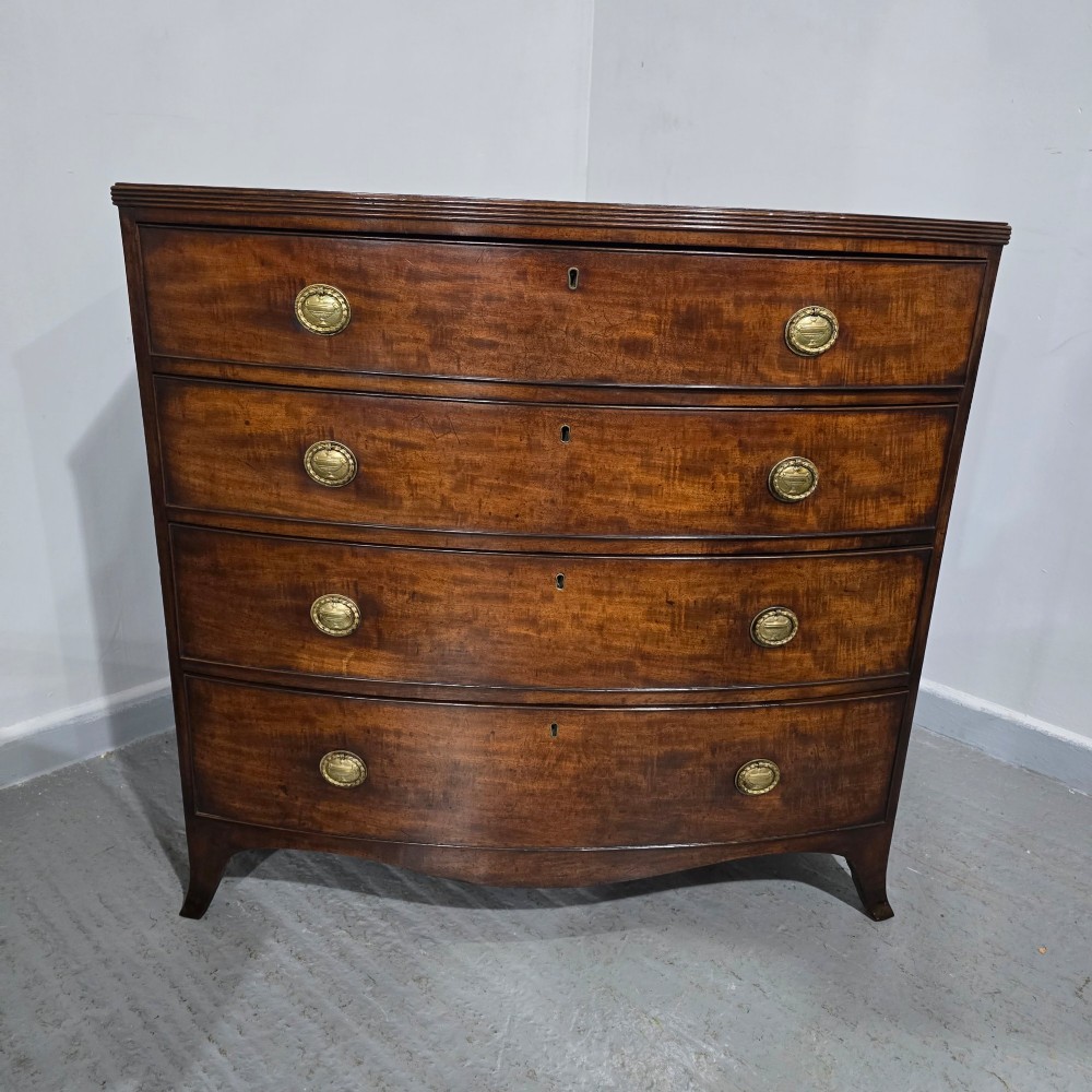 A Georgian mahogany bowfront chest of drawers featuring four graduated drawers with oval brass handles and splayed feet. View II