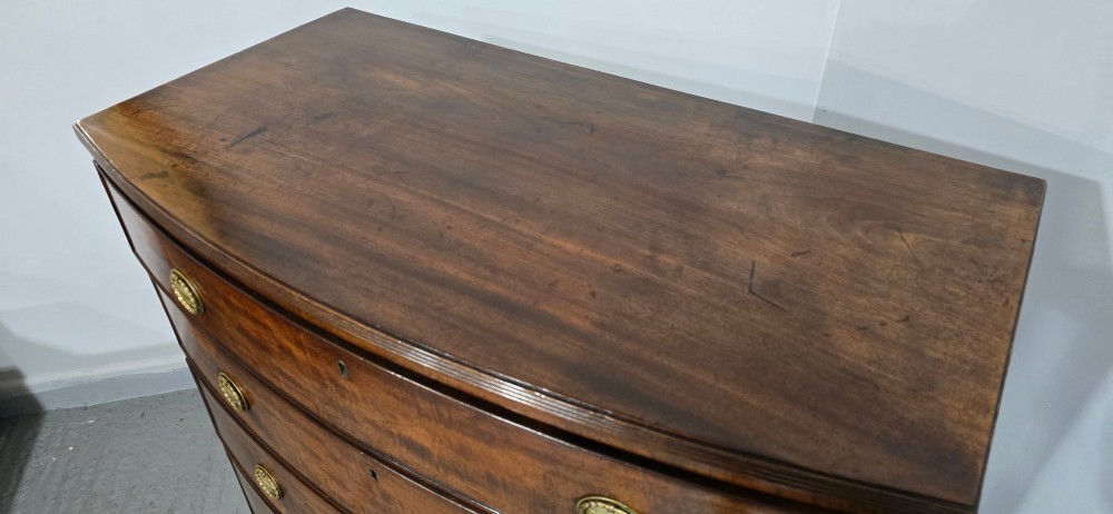 A Georgian mahogany bowfront chest of drawers featuring four graduated drawers with oval brass handles and splayed feet. View XIII