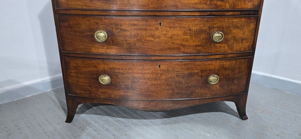A Georgian mahogany bowfront chest of drawers featuring four graduated drawers with oval brass handles and splayed feet. View XV