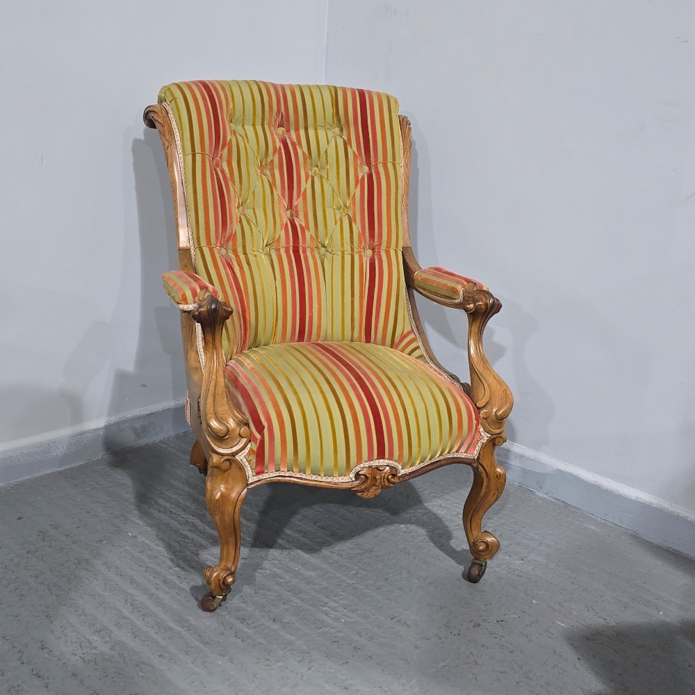 A Regency style rosewood library armchair with button-tufted striped upholstery, carved scroll arms, cabriole legs, and brass castors. View VI