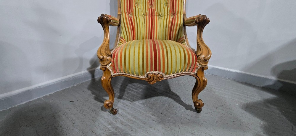 A Regency style rosewood library armchair with button-tufted striped upholstery, carved scroll arms, cabriole legs, and brass castors. View VII