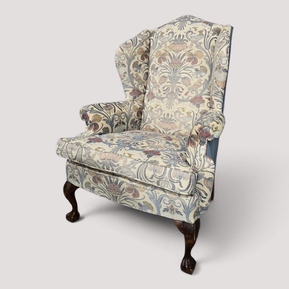 A high-backed wingback armchair upholstered in a botanical pattern with dark carved cabriole legs and ball-and-claw feet.