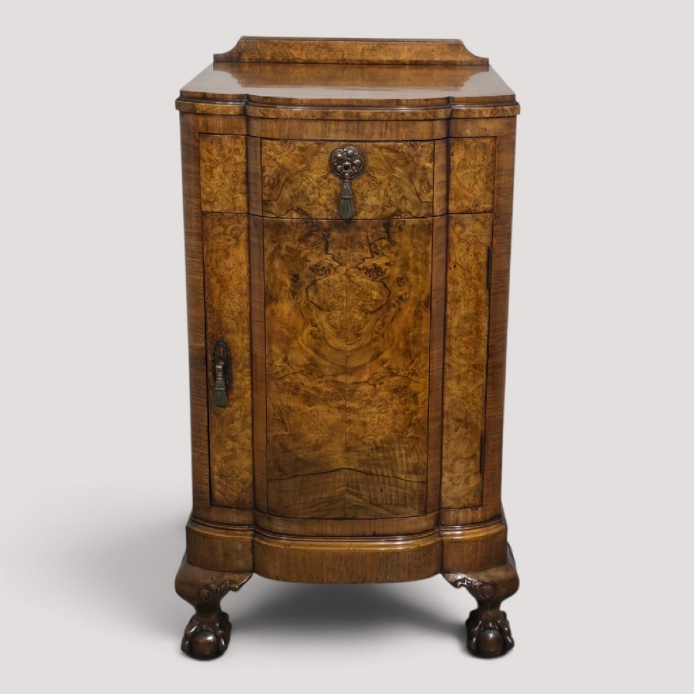 A small burr walnut side cabinet with a single upper drawer over a cupboard door, raised on carved cabriole legs with claw-and-ball feet.