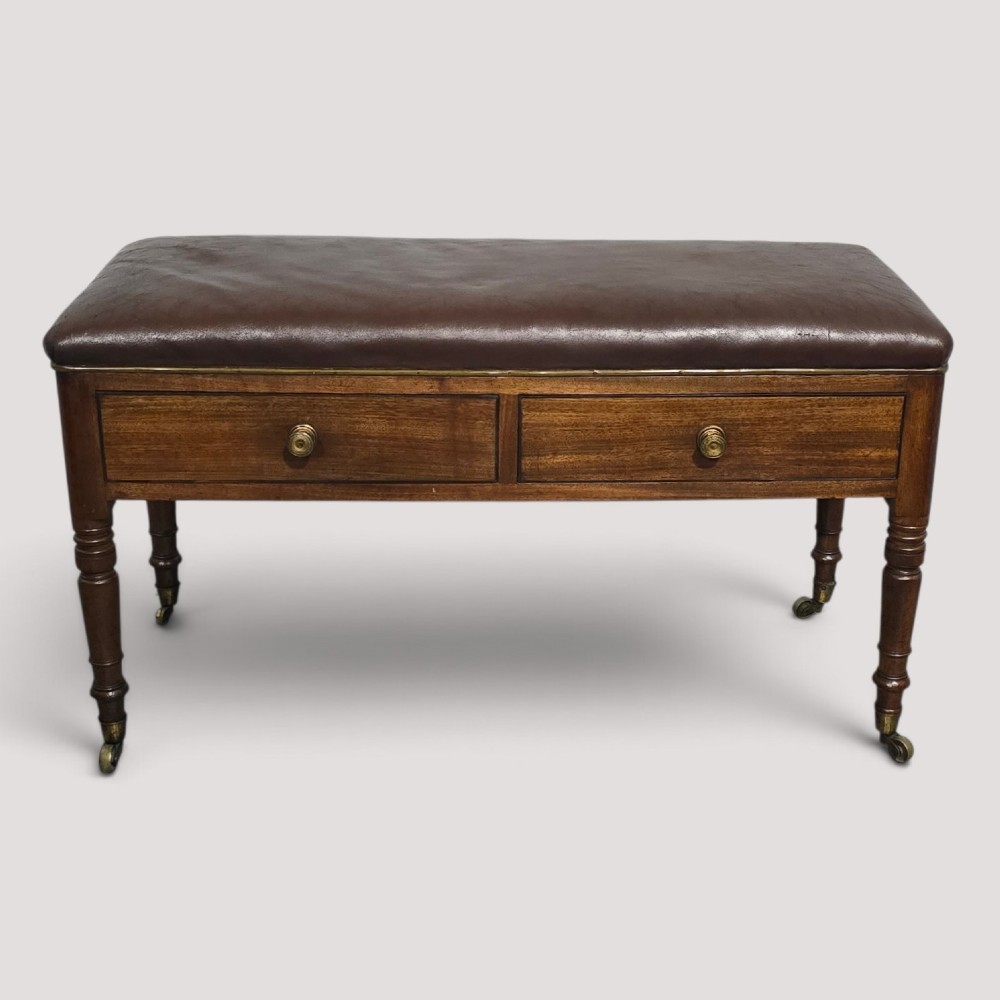 A Regency mahogany duet window stool with a brown leather seat, twin drawers, turned legs, and brass castors.