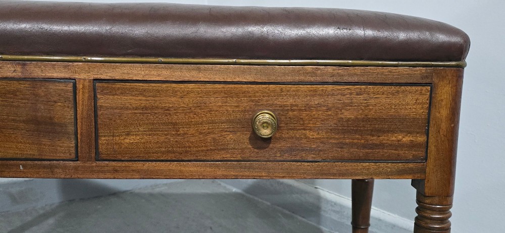A Regency mahogany duet window stool with a brown leather seat, twin drawers, turned legs, and brass castors. View V