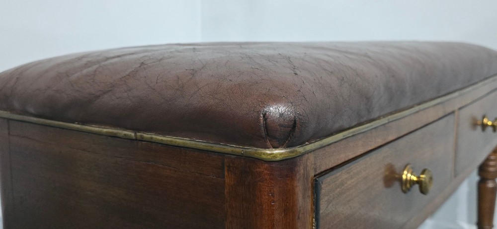 A Regency mahogany duet window stool with a brown leather seat, twin drawers, turned legs, and brass castors. View VII