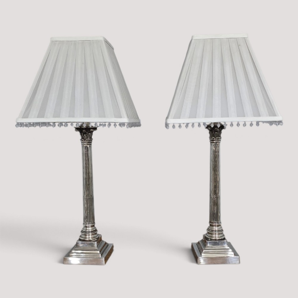 A pair of silver-plated neoclassical column table lamps with square stepped plinths and white pleated shades featuring beaded lower trim.