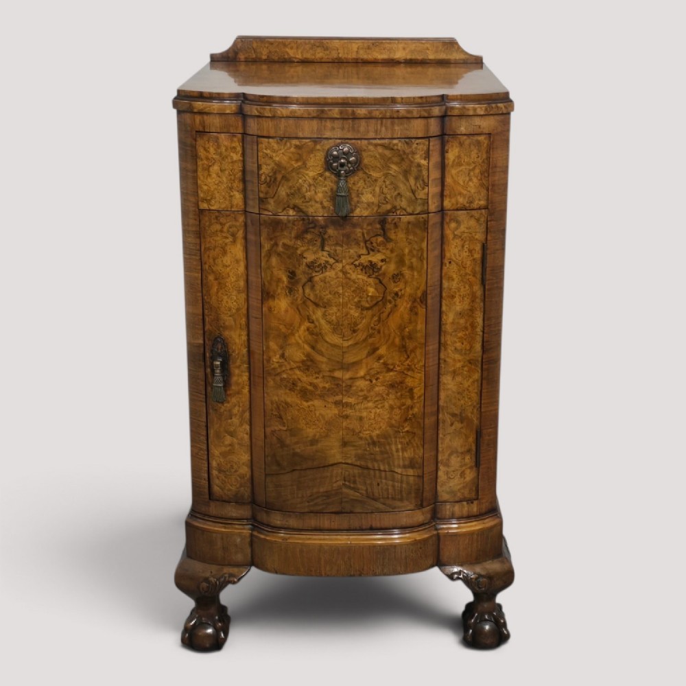 A burr walnut side cabinet with a bowed front, single drawer, cupboard door, and cabriole legs ending in carved claw and ball feet.