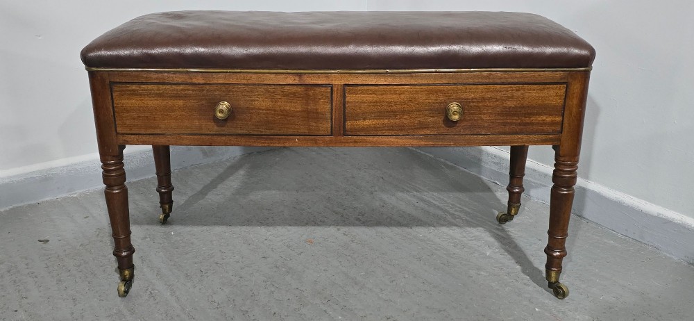 A Regency period mahogany duet stool with a brown leather upholstered top, two front frieze drawers with round brass knobs, and four turned legs on brass castors. View II