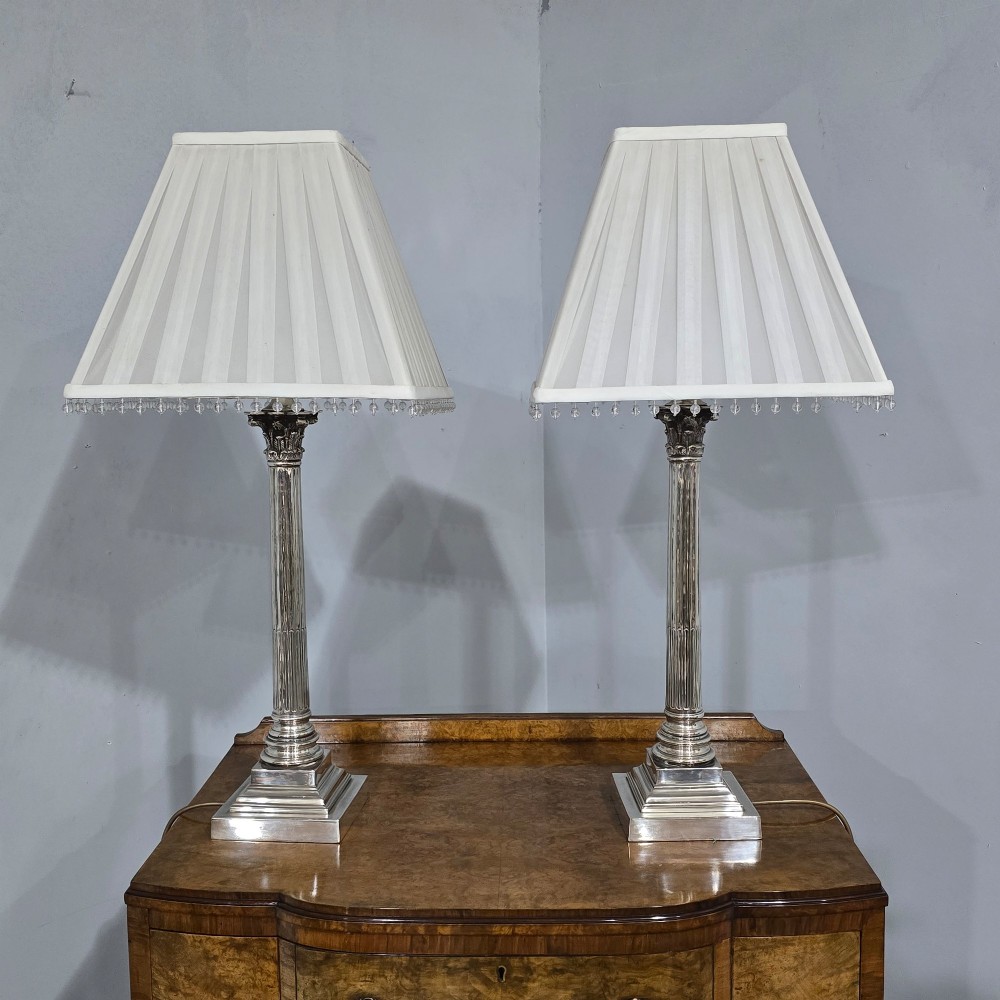 A pair of silver-plated table lamps styled as fluted Corinthian columns on stepped square bases, fitted with white pleated shades with beaded trim. View VI