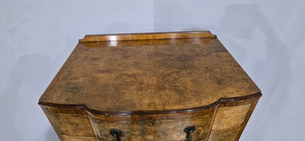 A two-section burr walnut linen press featuring a breakfront profile, upper drawers with drop handles, lower cupboard doors, and carved cabriole legs. View VII