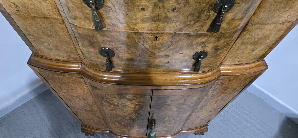 A two-section burr walnut linen press featuring a breakfront profile, upper drawers with drop handles, lower cupboard doors, and carved cabriole legs. View XI