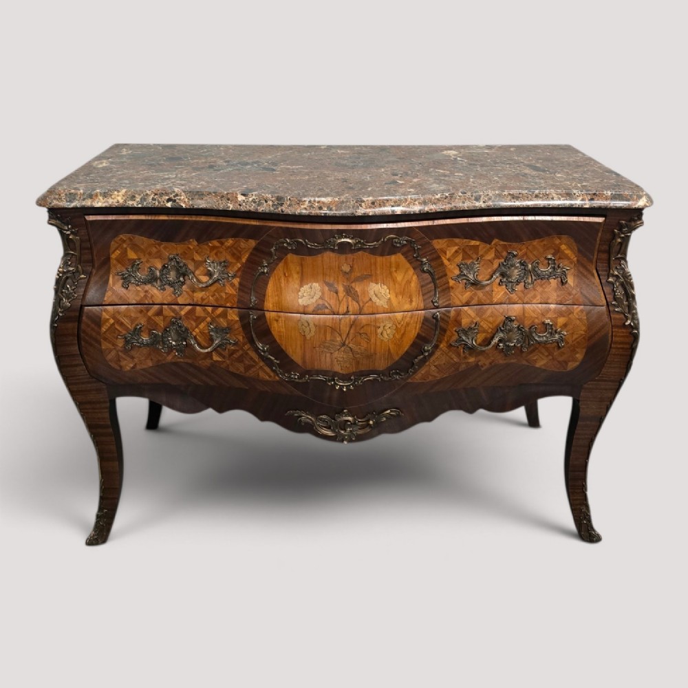 A French Louis XV style bombe commode featuring detailed floral marquetry inlay, bronze mounts, curved legs, and a brown marble top.