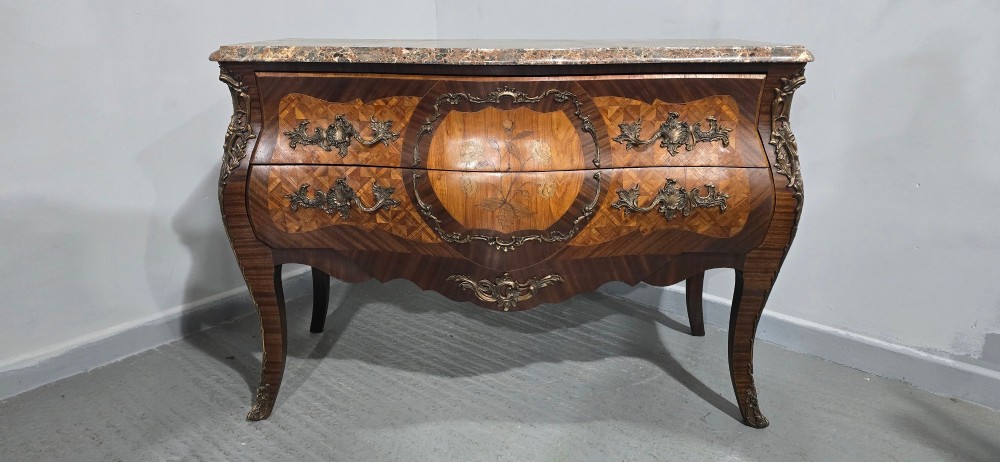 A French Louis XV style bombe commode featuring detailed floral marquetry inlay, bronze mounts, curved legs, and a brown marble top. View III