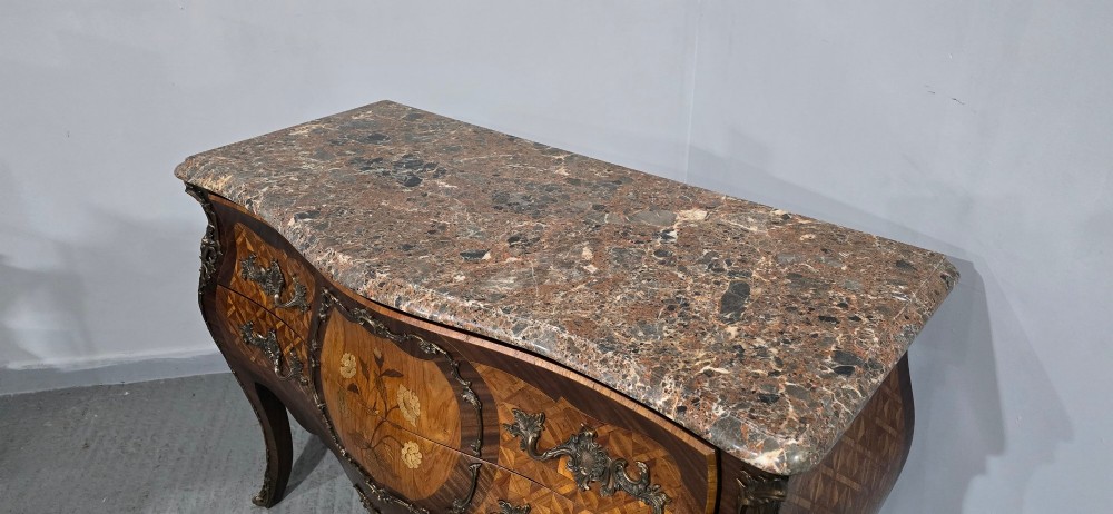 A French Louis XV style bombe commode featuring detailed floral marquetry inlay, bronze mounts, curved legs, and a brown marble top. View VIII