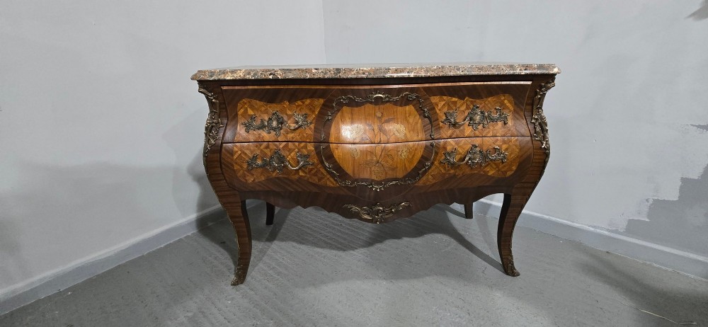 A French Louis XV style bombe commode featuring detailed floral marquetry inlay, bronze mounts, curved legs, and a brown marble top. View XIV