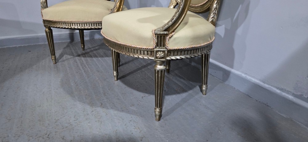 A pair of French Louis XVI style open armchairs featuring carved giltwood frames with oval medallion backs, fluted legs, and neutral cream upholstery. View VIII