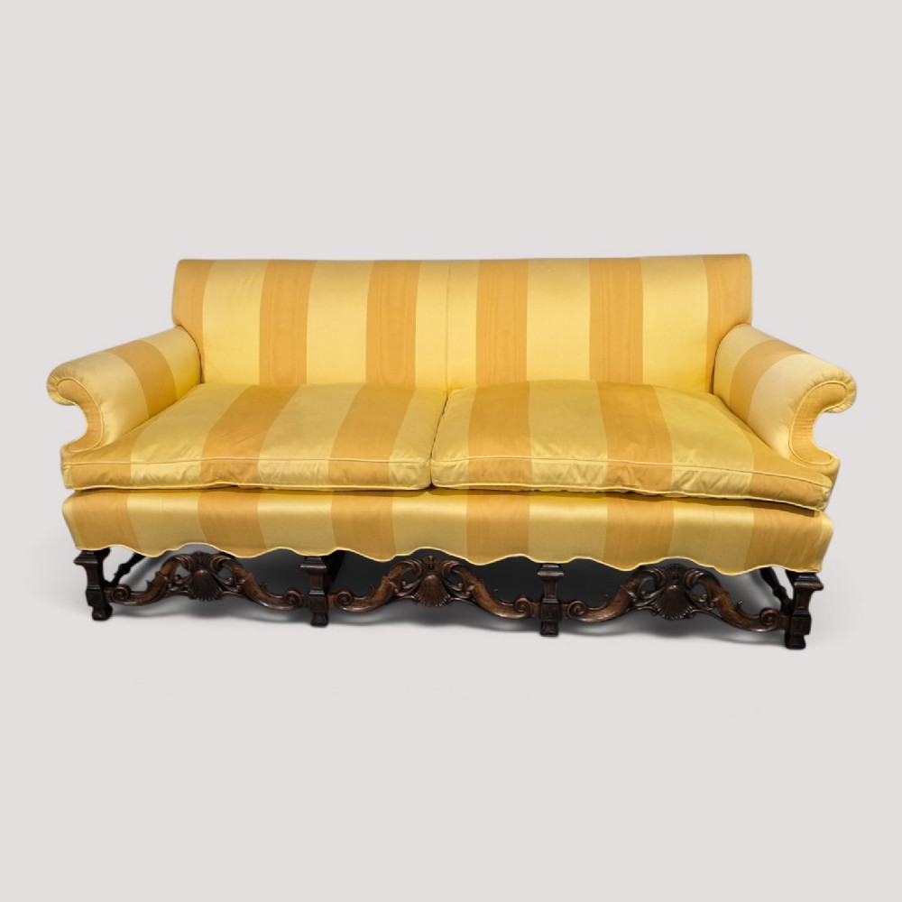 An upholstered sofa featuring yellow and gold vertical stripes with an intricately carved dark oak base decorated with shell motifs and scrolls.