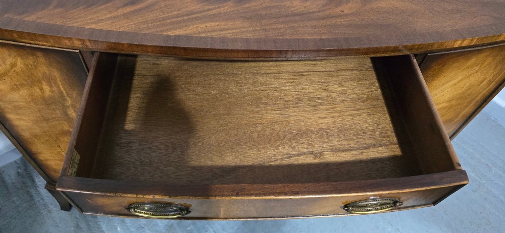 A bow-front mahogany sideboard featuring four central drawers flanked by two side cupboard doors with oval brass handles and flame mahogany grain patterns. View IX