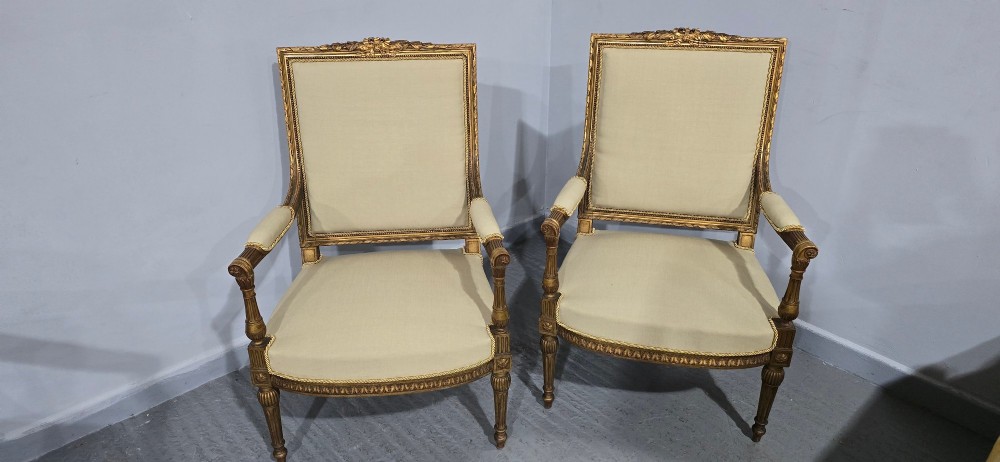 A pair of French Neoclassical giltwood open armchairs upholstered in neutral fabric with fluted tapered legs and carved square backs. View III