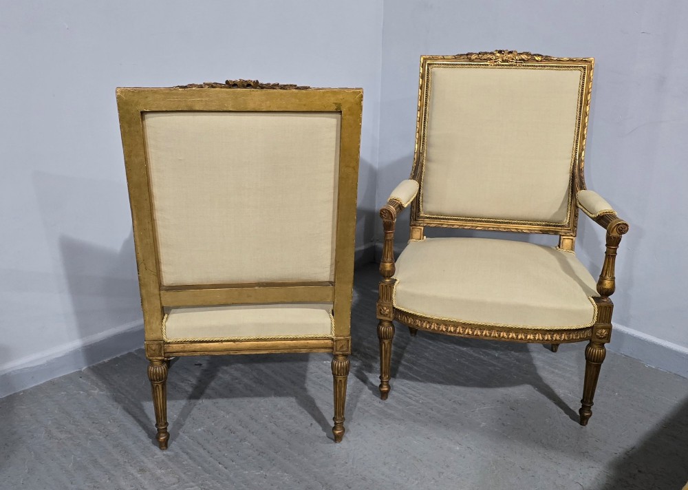 A pair of French Neoclassical giltwood open armchairs upholstered in neutral fabric with fluted tapered legs and carved square backs. View XI