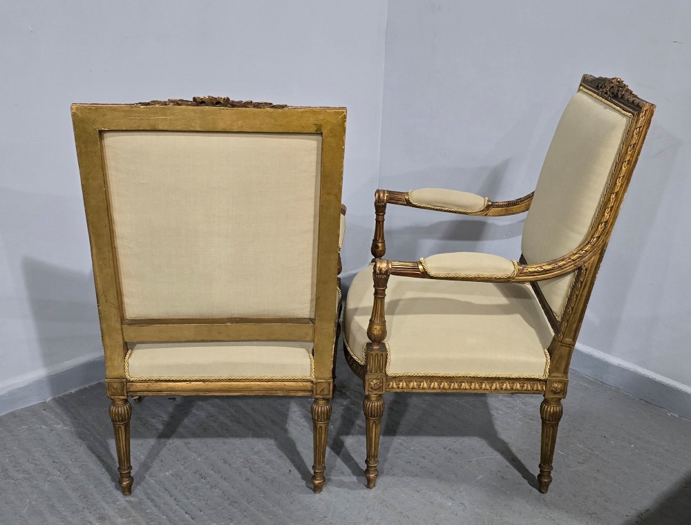 A pair of French Neoclassical giltwood open armchairs upholstered in neutral fabric with fluted tapered legs and carved square backs. View XII
