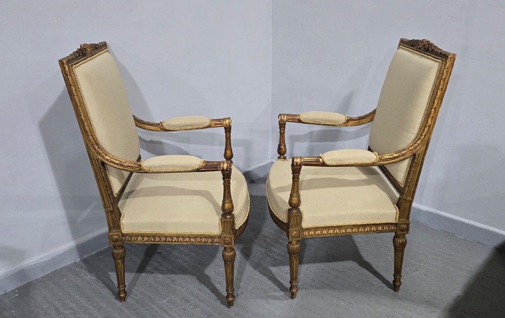 A pair of French Neoclassical giltwood open armchairs upholstered in neutral fabric with fluted tapered legs and carved square backs. View XIII