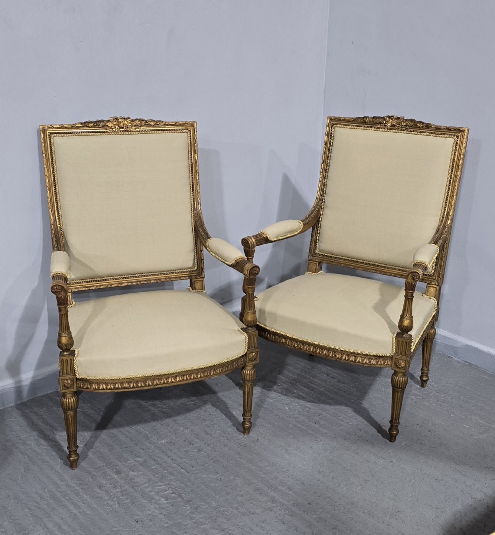 A pair of French Neoclassical giltwood open armchairs upholstered in neutral fabric with fluted tapered legs and carved square backs. View XIV