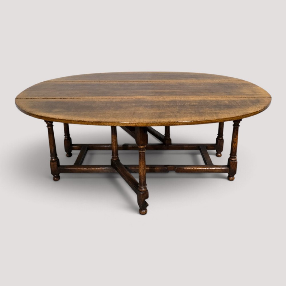 A large oval solid oak wake table featuring drop-leaf sides, turned legs, and square stretchers.