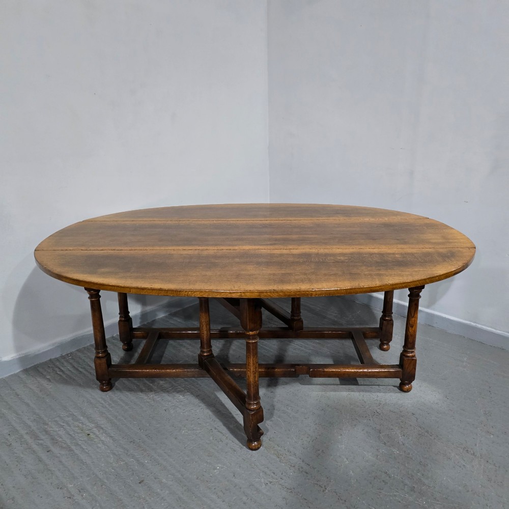 A large oval solid oak wake table featuring drop-leaf sides, turned legs, and square stretchers. View II