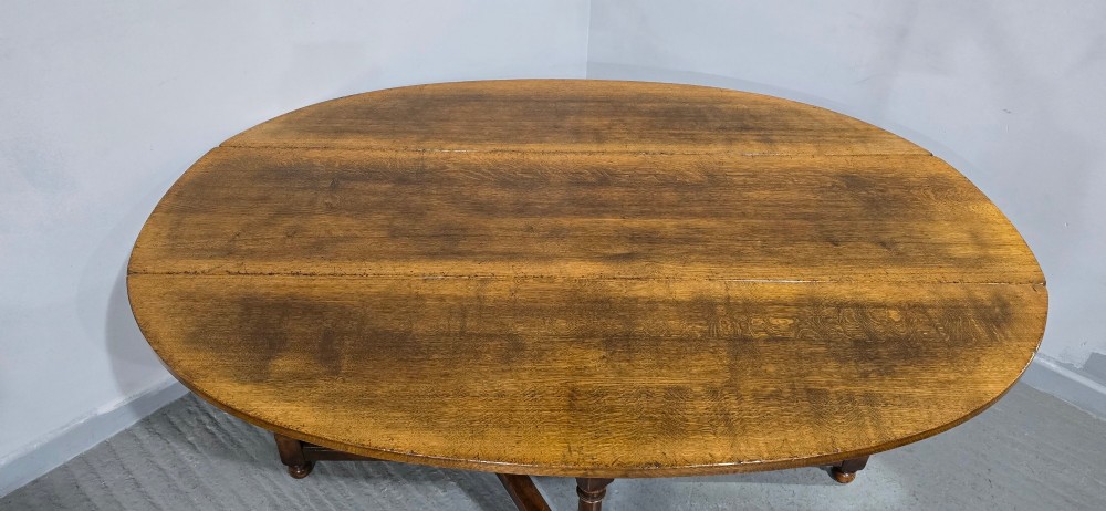 A large oval solid oak wake table featuring drop-leaf sides, turned legs, and square stretchers. View III