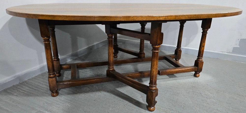 A large oval solid oak wake table featuring drop-leaf sides, turned legs, and square stretchers. View IV