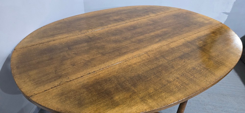 A large oval solid oak wake table featuring drop-leaf sides, turned legs, and square stretchers. View V