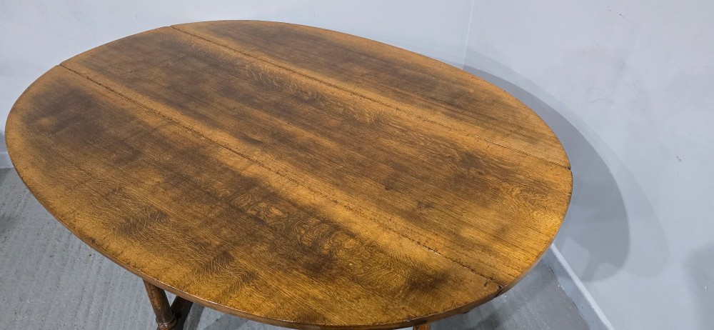A large oval solid oak wake table featuring drop-leaf sides, turned legs, and square stretchers. View VI