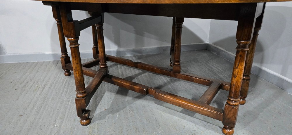 A large oval solid oak wake table featuring drop-leaf sides, turned legs, and square stretchers. View VII
