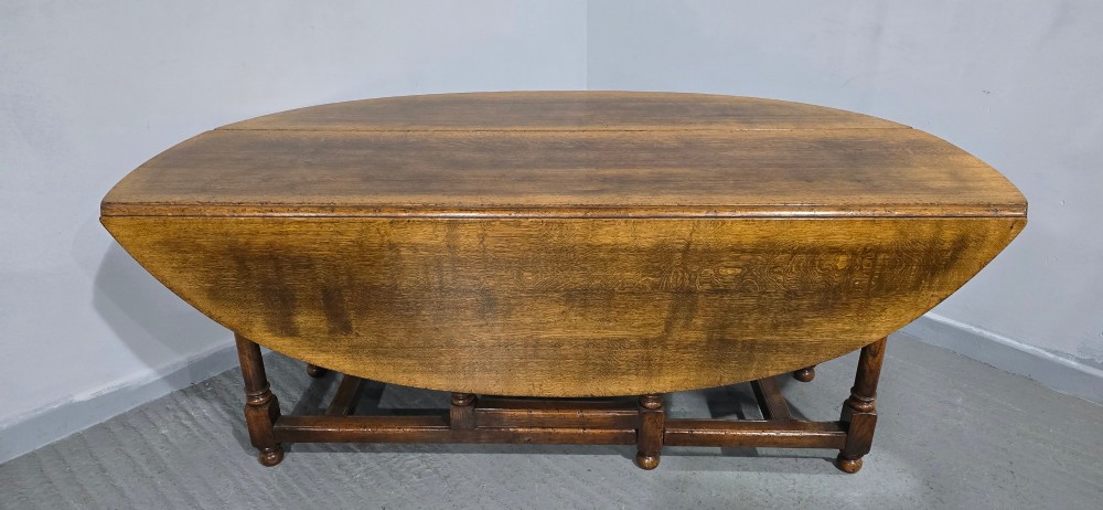 A large oval solid oak wake table featuring drop-leaf sides, turned legs, and square stretchers. View IX