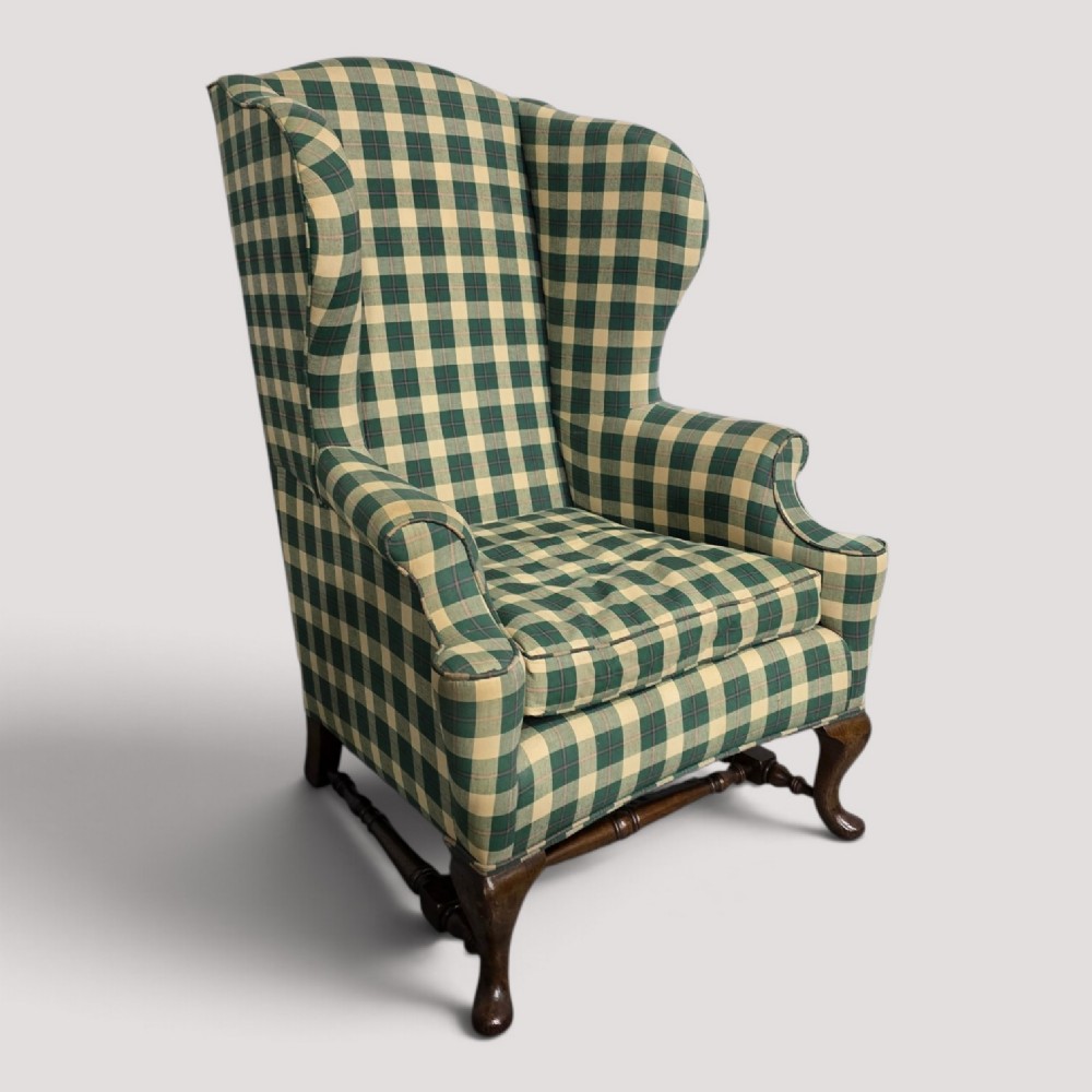 High-backed wingback armchair upholstered in green and cream check fabric with carved oak cabriole front legs.