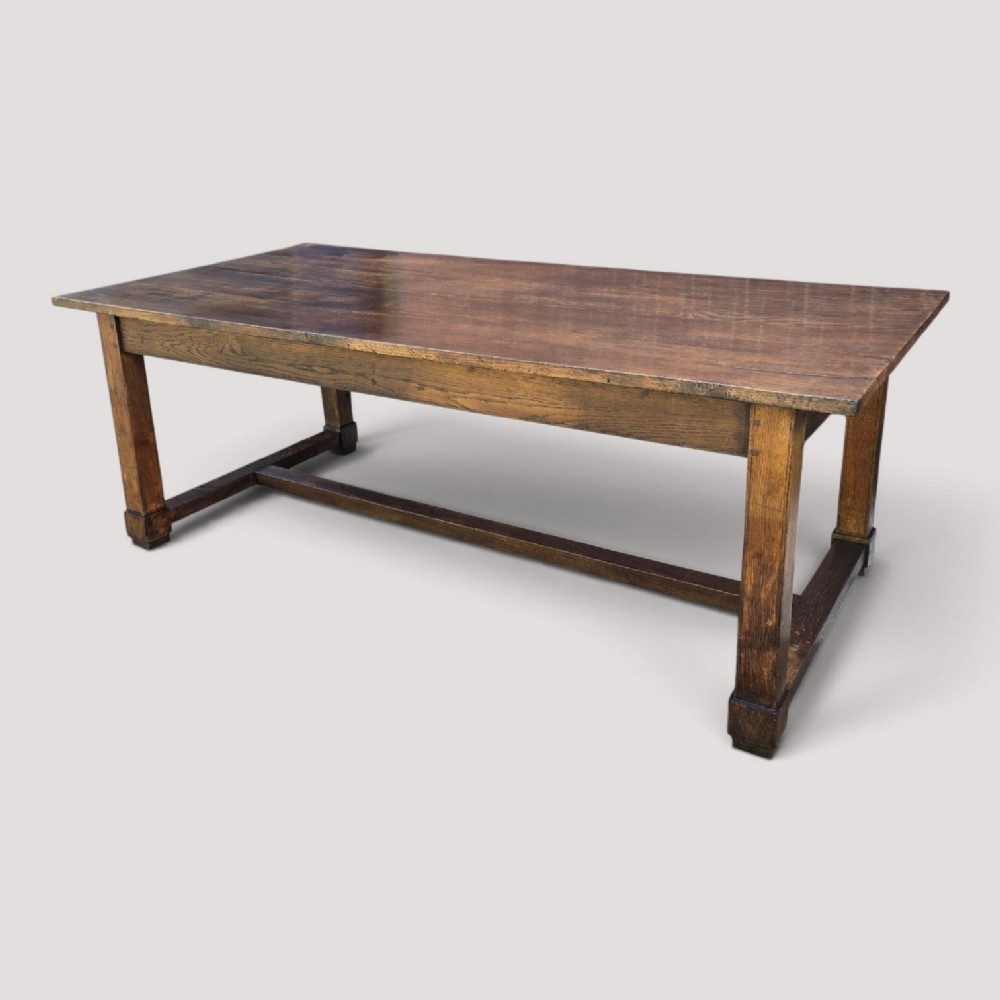 A solid warm brown French oak refectory dining table featuring a rectangular plank top, square legs, and an H-stretcher base. View III
