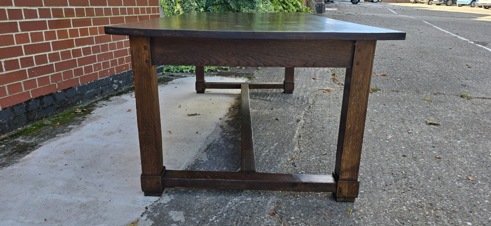 A solid warm brown French oak refectory dining table featuring a rectangular plank top, square legs, and an H-stretcher base. View IV