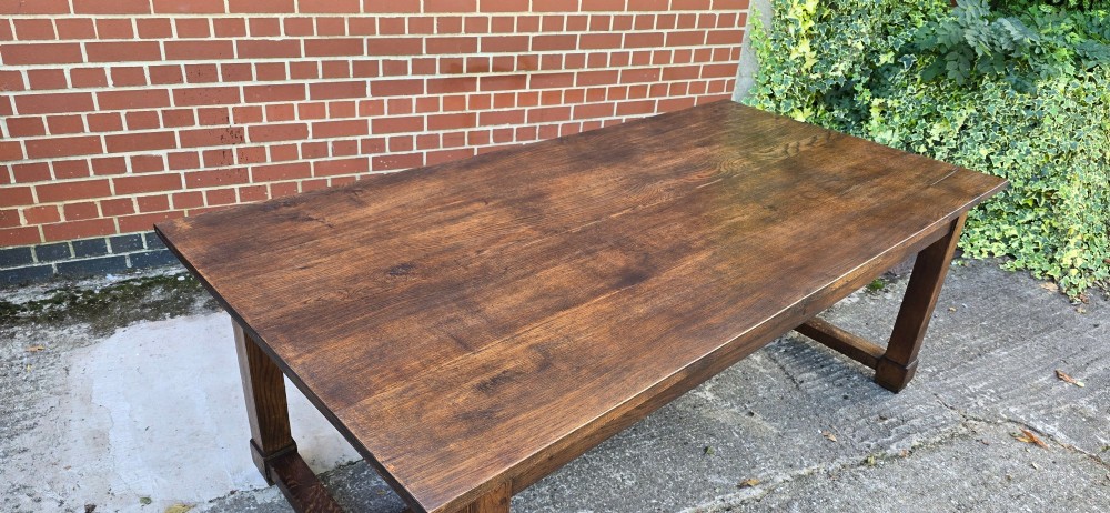A solid warm brown French oak refectory dining table featuring a rectangular plank top, square legs, and an H-stretcher base. View VII