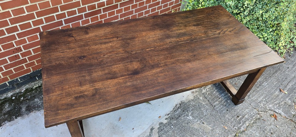 A solid warm brown French oak refectory dining table featuring a rectangular plank top, square legs, and an H-stretcher base. View X