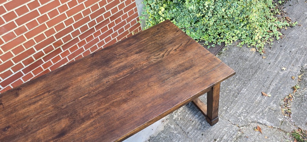 A solid warm brown French oak refectory dining table featuring a rectangular plank top, square legs, and an H-stretcher base. View XIV