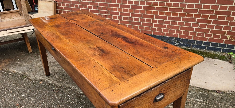 A rectangular French cherry wood refectory dining table featuring a three-plank top, side frieze drawer with metal handle, and square tapered legs. View V