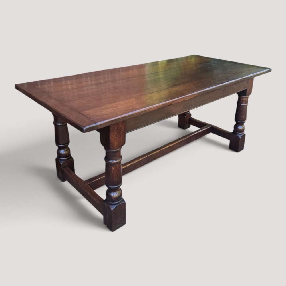 A solid dark oak refectory dining table with a plank top, stout turned legs, and an H-stretcher base.