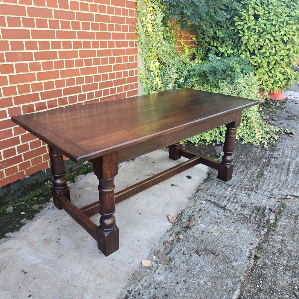 A solid dark oak refectory dining table with a plank top, stout turned legs, and an H-stretcher base. View II