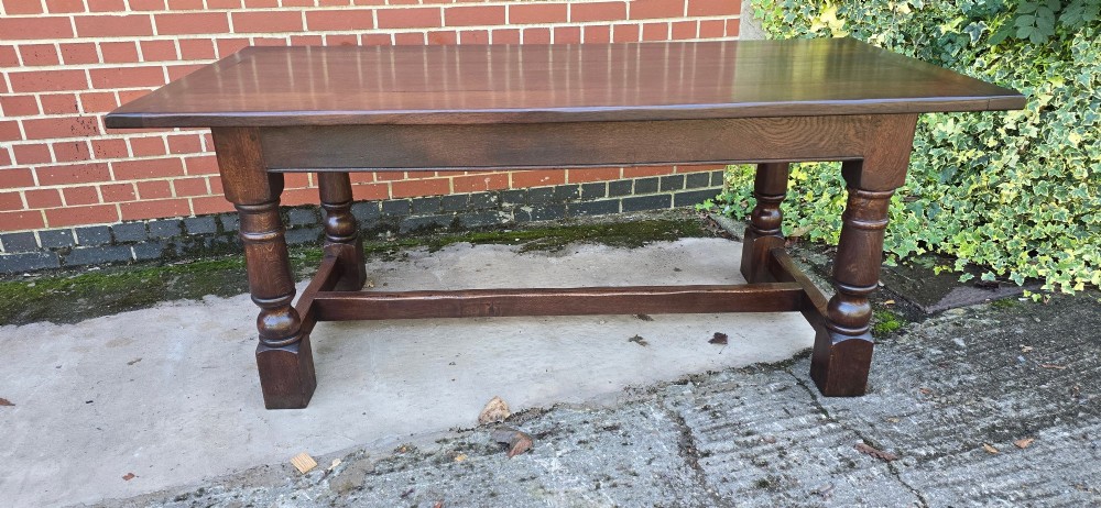 A solid dark oak refectory dining table with a plank top, stout turned legs, and an H-stretcher base. View III
