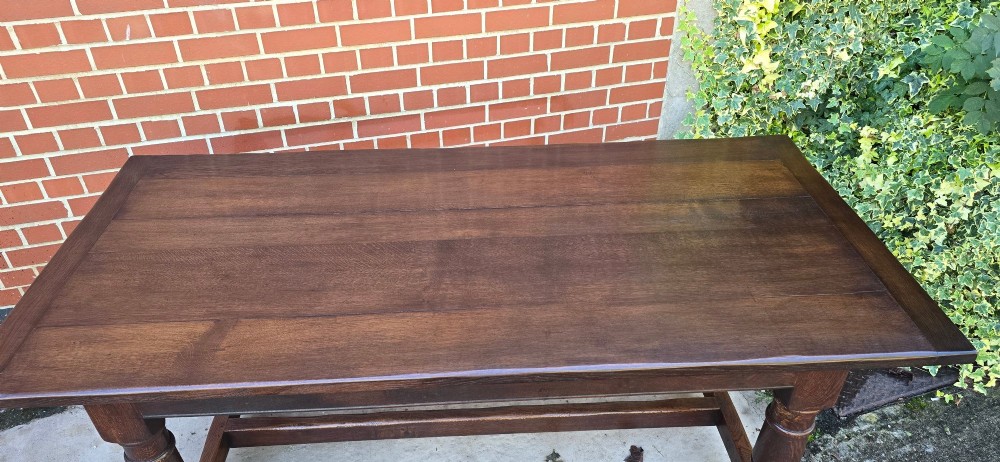 A solid dark oak refectory dining table with a plank top, stout turned legs, and an H-stretcher base. View IV